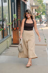 Woman walking on a sidewalk wearing a brown top and beige pants.